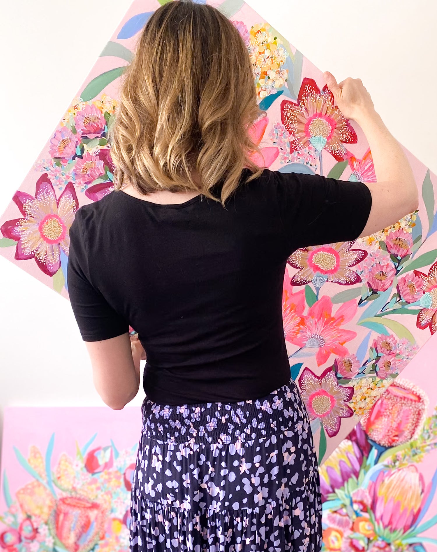 Rachelle Holowko arranging colourful floral original acrylic artwork on a wall.