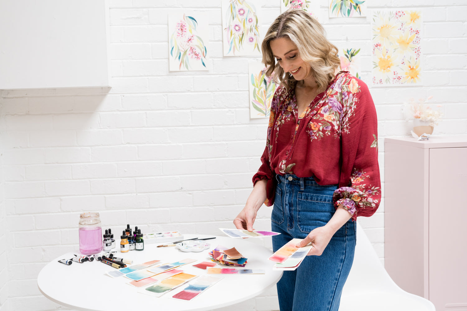 Rachelle Holowko in a floral blouse and jeans, standing at a table looking at colour swatches